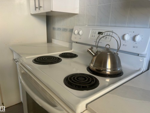 The kitchen features white cabinetry, a white electric range, and tiled backsplash - 14911 77 Street Nw, Edmonton, AB - Indoor Photo Showing Kitchen