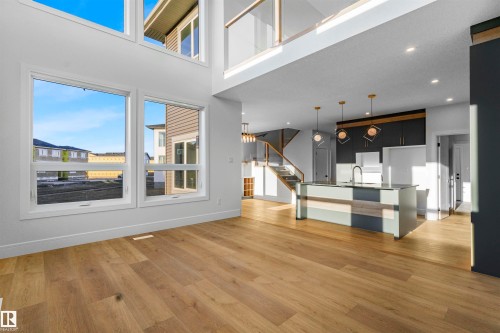Expansive living area featuring hardwood floors, high ceilings, large windows, and an open-concept kitchen with a central island and contemporary light fixtures - 368 Creekside Green, Leduc, AB - Indoor
