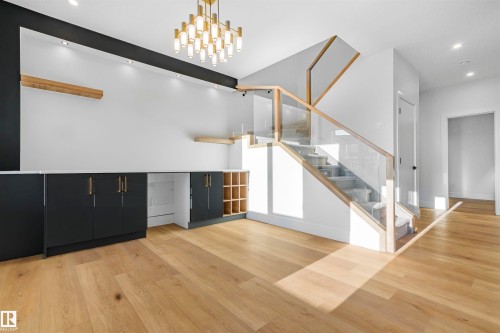 This inviting space features light-toned hardwood flooring, a modern staircase with glass and wood railings, and a contemporary chandelier - 368 Creekside Green, Leduc, AB - Indoor Photo Showing Other Room