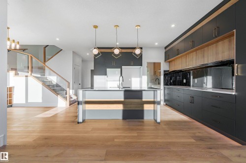 Contemporary kitchen featuring dark cabinetry, light wood accents, an island with a sink, and pendant lighting - 368 Creekside Green, Leduc, AB - Indoor Photo Showing Kitchen With Upgraded Kitchen