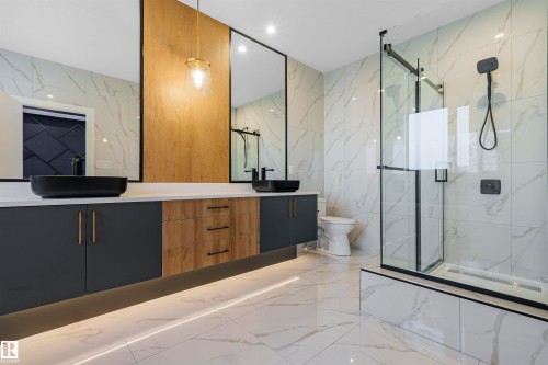 Bathroom featuring a dual vanity with black vessel sinks, a glass-enclosed shower, and marble-look tiled walls and flooring - 368 Creekside Green, Leduc, AB - Indoor Photo Showing Bathroom