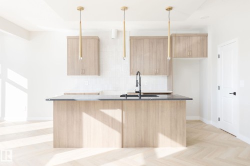 The kitchen features a central island with a sink and a dark countertop, complemented by light wood cabinetry - 2206 Crossbill Link, Edmonton, AB - Indoor Photo Showing Kitchen