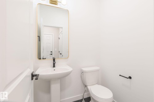 This bathroom features a pedestal sink with a matte black faucet, a toilet, and a gold-framed mirror with an overhead light fixture - 2206 Crossbill Link, Edmonton, AB - Indoor Photo Showing Bathroom