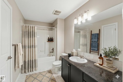 Bathroom featuring a dark vanity with a white oval sink, a large mirror with overhead lighting, a white bathtub with a shower, and light-colored walls - 5014 Dewolf Road, Edmonton, AB 