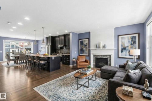Spacious open concept living area featuring hardwood floors, a kitchen island with seating, dark cabinetry, and a fireplace with a stone surround - 5014 Dewolf Road, Edmonton, AB 