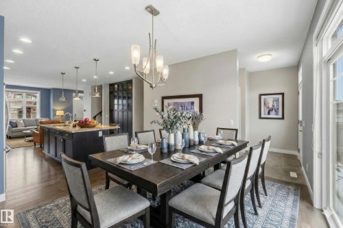 The dining area features a large table with seating, an elegant chandelier, and natural light from a window - 5014 Dewolf Road, Edmonton, AB 
