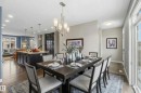 The dining area features a large table with seating, an elegant chandelier, and natural light from a window - 5014 Dewolf Road, Edmonton, AB 
