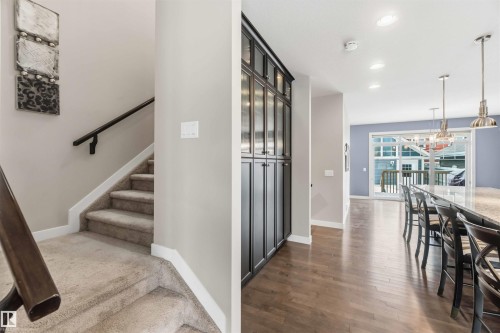 This property features a carpeted staircase with a dark wood handrail, alongside a spacious living area with hardwood flooring - 5014 Dewolf Road, Edmonton, AB 