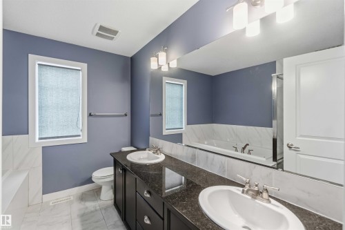 Well-appointed bathroom featuring a dual vanity with dark countertops, a large mirror, and a window with a roller blind - 5014 Dewolf Road, Edmonton, AB 
