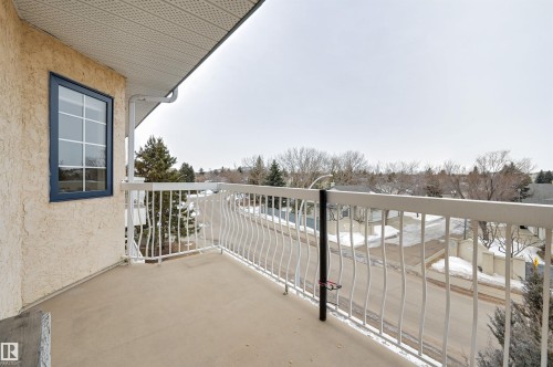 The property features a private balcony with a white railing, offering views of the surrounding neighborhood with trees and a street - 304 17151 94A Avenue, Edmonton, AB - Outdoor With Balcony With Exterior