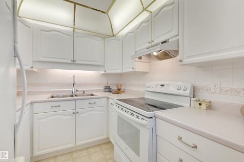 The kitchen features white cabinetry, a white countertop, and a white electric range with a cooktop - 304 17151 94A Avenue, Edmonton, AB - Indoor Photo Showing Kitchen With Double Sink