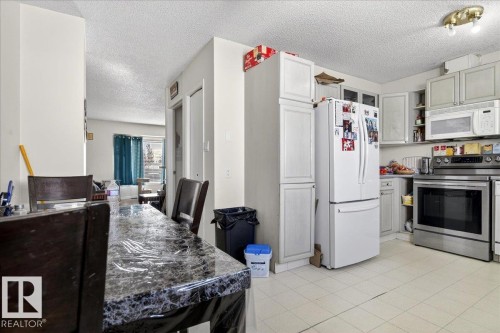 The kitchen features white cabinetry, a white refrigerator, and stainless steel appliances including a range with an overhead microwave - 13304 130 Avenue, Edmonton, AB - Indoor Photo Showing Kitchen