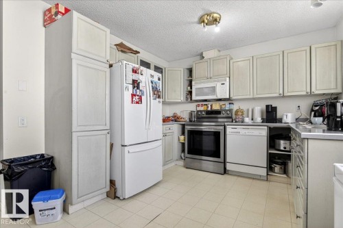 The kitchen features extensive cabinetry, a double-door refrigerator, a microwave, and a dishwasher, all set against tiled flooring - 13304 130 Avenue, Edmonton, AB - Indoor Photo Showing Kitchen