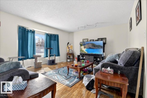 Living space featuring hardwood flooring, light-colored walls, and a large window with blue curtains - 13304 130 Avenue, Edmonton, AB - Indoor Photo Showing Living Room