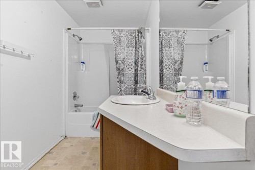 Bathroom featuring a vanity with an integrated sink and mirror, and a shower-over-tub combination with a shower curtain - 13304 130 Avenue, Edmonton, AB - Indoor Photo Showing Bathroom