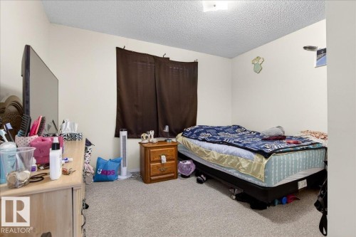 This room features neutral-toned walls and carpeting, with a window fitted with dark brown curtains - 13304 130 Avenue, Edmonton, AB - Indoor Photo Showing Bedroom