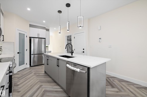The kitchen features a large island with a sink, stainless steel appliances, and herringbone-patterned flooring - 8321 81Ave, Edmonton, AB - Indoor Photo Showing Kitchen With Double Sink With Upgraded Kitchen