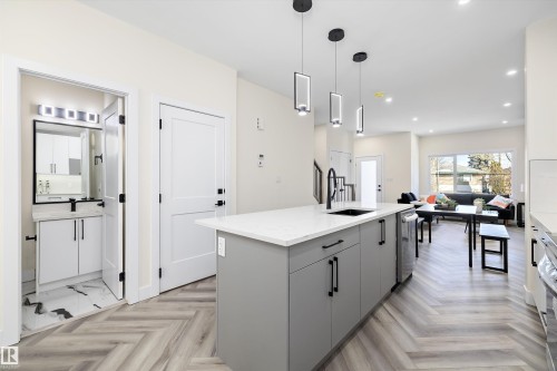 The kitchen features a large island with a white countertop and a sink, complemented by modern pendant lighting overhead - 8321 81Ave, Edmonton, AB - Indoor Photo Showing Kitchen With Upgraded Kitchen