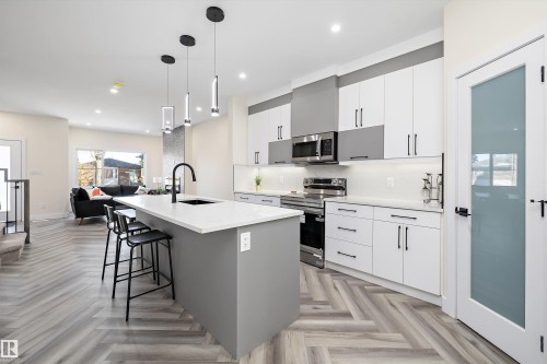 The kitchen features a large island with a white countertop and a black sink, pendant lighting, and stainless steel appliances - 8321 81Ave, Edmonton, AB - Indoor Photo Showing Kitchen With Upgraded Kitchen