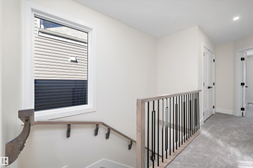 The property features a staircase with a wooden handrail and black metal balusters, and a window with white trim, set against light-colored walls - 8321 81Ave, Edmonton, AB - Indoor Photo Showing Other Room
