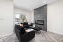 The living area features a modern electric fireplace with a stone accent wall, large windows, recessed lighting, and herringbone pattern flooring - 8321 81Ave, Edmonton, AB  - Indoor Photo Showing Living Room With Fireplace 