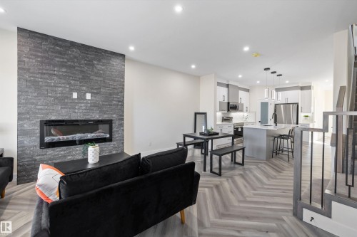 This open concept living space features a striking floor-to-ceiling stone-clad fireplace and light-toned chevron pattern flooring throughout - 8321 81Ave, Edmonton, AB - Indoor Photo Showing Living Room With Fireplace
