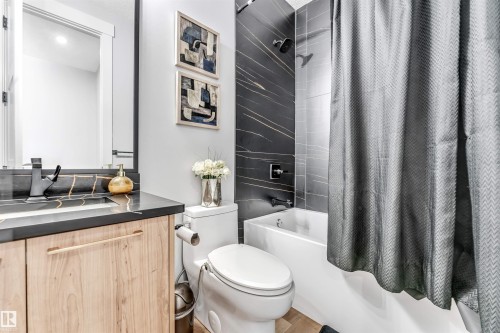 The bathroom features a vanity with a dark countertop and a light wood-toned cabinet, a toilet, and a bathtub with dark tiled walls - 1531 151 Avenue, Edmonton, AB - Indoor Photo Showing Bathroom
