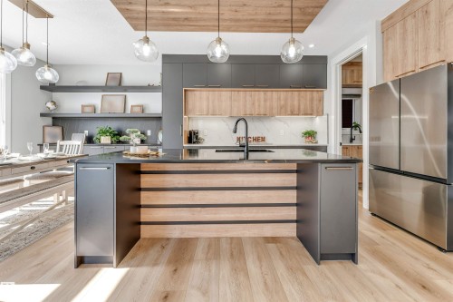 The kitchen and dining area features light wood flooring, a central island with a dark countertop and integrated sink, and stainless steel appliances - 1531 151 Avenue, Edmonton, AB - Indoor Photo Showing Kitchen With Upgraded Kitchen