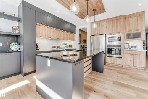 Modern kitchen featuring an island with a black countertop and a sink with a black faucet, light wood flooring, and light wood cabinetry with stainless steel appliances - 1531 151 Avenue, Edmonton, AB - Indoor Photo Showing Kitchen With Upgraded Kitchen