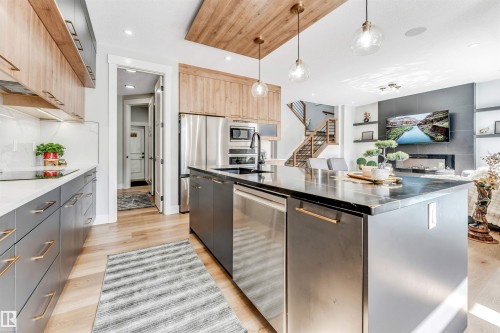 The kitchen features hardwood floors, a large island with a dark countertop, and stainless steel appliances, including a dishwasher and refrigerator - 1531 151 Avenue, Edmonton, AB - Indoor Photo Showing Kitchen With Upgraded Kitchen