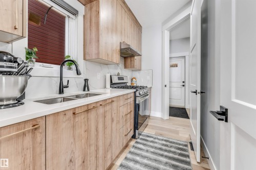 The kitchen features light wood cabinetry, white countertops, and a double basin sink with a black faucet - 1531 151 Avenue, Edmonton, AB - Indoor Photo Showing Kitchen With Double Sink