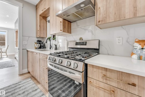 Modern kitchen featuring light wood cabinetry, white countertops, a stainless steel range with a matching range hood, and a marble-patterned backsplash - 1531 151 Avenue, Edmonton, AB - Indoor Photo Showing Kitchen