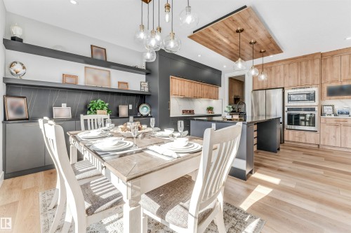 The kitchen features light wood flooring, stainless steel appliances, a center island with a dark countertop, and a wooden ceiling accent with pendant lighting - 1531 151 Avenue, Edmonton, AB - Indoor Photo Showing Dining Room