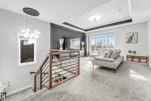 This inviting living area features soft carpeting, a large window offering natural light, and a stylish ceiling light fixture - 1531 151 Avenue, Edmonton, AB - Indoor