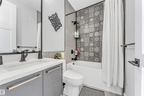 Bathroom featuring a vanity with a white countertop and grey cabinetry, a bathtub with a patterned tile surround, and matte black fixtures - 1531 151 Avenue, Edmonton, AB - Indoor Photo Showing Bathroom
