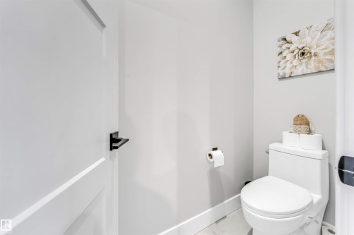 Bathroom featuring a white toilet with a matching toilet paper holder and a white door with a black handle - 1531 151 Avenue, Edmonton, AB - Indoor Photo Showing Bathroom