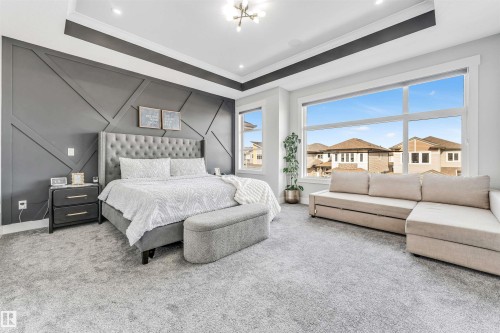 This bedroom features a stylish accent wall with geometric paneling, large windows offering natural light, and plush grey carpeting - 1531 151 Avenue, Edmonton, AB - Indoor Photo Showing Bedroom