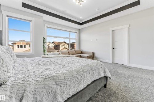 This spacious room features large windows providing ample natural light, soft grey carpeting, and a tray ceiling with a dark accent band - 1531 151 Avenue, Edmonton, AB - Indoor Photo Showing Bedroom