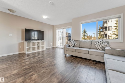 The property features dark wood-style flooring, light-colored walls, and a window with a pleasant view of evergreen trees and other buildings - 1624 33A Street, Edmonton, AB - Indoor Photo Showing Living Room