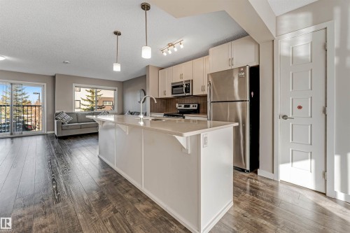 Open concept living area featuring dark wood-style flooring, a kitchen island with a light-colored countertop, and a kitchen equipped with stainless steel appliances and light-colored cabinetry - 1624 33A Street, Edmonton, AB - Indoor Photo Showing Kitchen With Double Sink