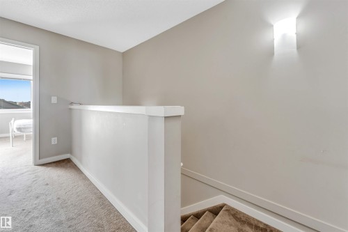 Carpeted hallway with a wall-mounted light fixture and a staircase featuring carpeted treads - 1624 33A Street, Edmonton, AB - Indoor Photo Showing Other Room