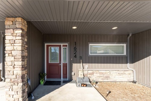 The property features an inviting entrance with a deep red door, vertical siding, and a stone column - 1624 33A Street, Edmonton, AB - Outdoor