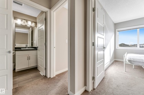 The property features a bathroom with a vanity, mirror, and overhead lighting, alongside a room with a window and carpeted flooring - 1624 33A Street, Edmonton, AB - Indoor
