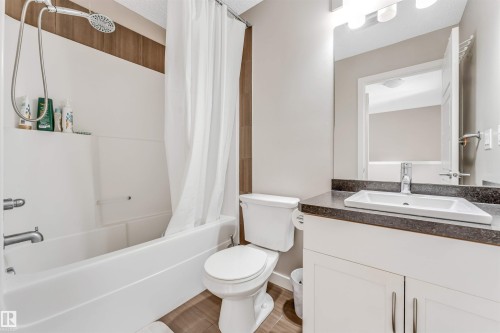 Bathroom featuring a white bathtub with a shower head, a white toilet, and a vanity with a dark countertop and white cabinetry - 1624 33A Street, Edmonton, AB - Indoor Photo Showing Bathroom
