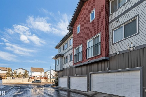 The property features a contemporary exterior with red and grey siding, balconies with black railings, and integrated garages with white doors - 1624 33A Street, Edmonton, AB - Outdoor