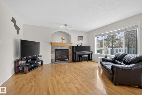 Living room featuring hardwood floors, a fireplace with a tiled surround, and a large window providing natural light - 1119 Rutherford Close, Edmonton, AB - Indoor Photo Showing Living Room With Fireplace