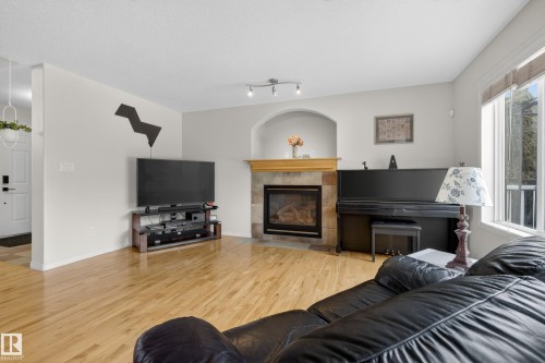 Living area featuring hardwood floors, a stone-tiled fireplace with a wood mantel, and a window providing natural light - 1119 Rutherford Close, Edmonton, AB - Indoor Photo Showing Living Room With Fireplace