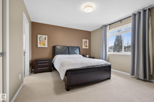 This room features light-colored carpeting, a window with curtains providing natural light, and a brown accent wall - 1119 Rutherford Close, Edmonton, AB - Indoor Photo Showing Bedroom