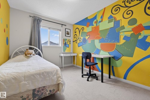 This room features light-colored carpeting, a window with grey curtains, and walls with vibrant, artistic murals - 1119 Rutherford Close, Edmonton, AB - Indoor Photo Showing Bedroom
