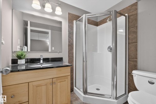 Bathroom with a light wood vanity, dark countertop, and a corner shower with a glass enclosure - 1119 Rutherford Close, Edmonton, AB - Indoor Photo Showing Bathroom